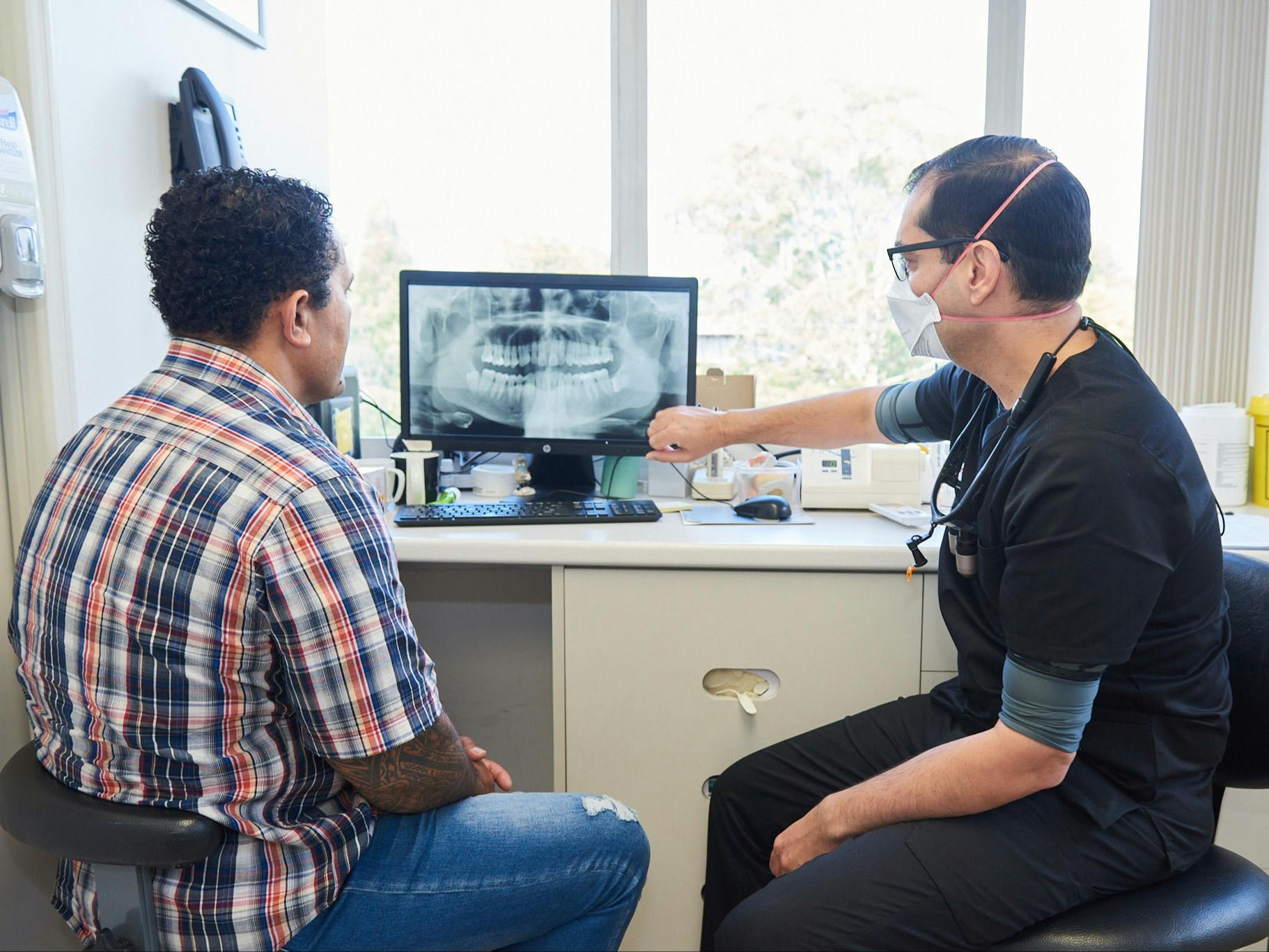 photo of a male dentist showing dental x-ray on a computer screen to male patient 