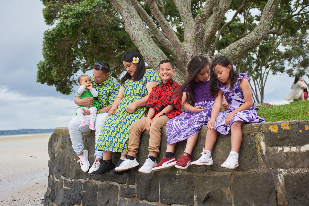 Samoan family with baby sitting on wall at park beside beach